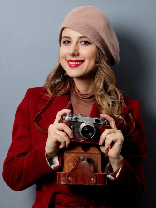 young-woman-in-red-coat-with-camera-on-grey-background-e1647503915654.jpg